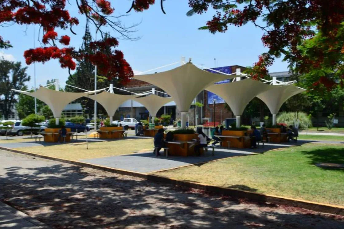 Zona de estudio al aire libre del campus, con mesas bajo las tensoestructuras