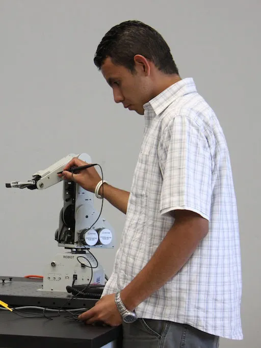 Estudiante de CUCEI ajustando un brazo robótico didáctico junto a un osciloscopio